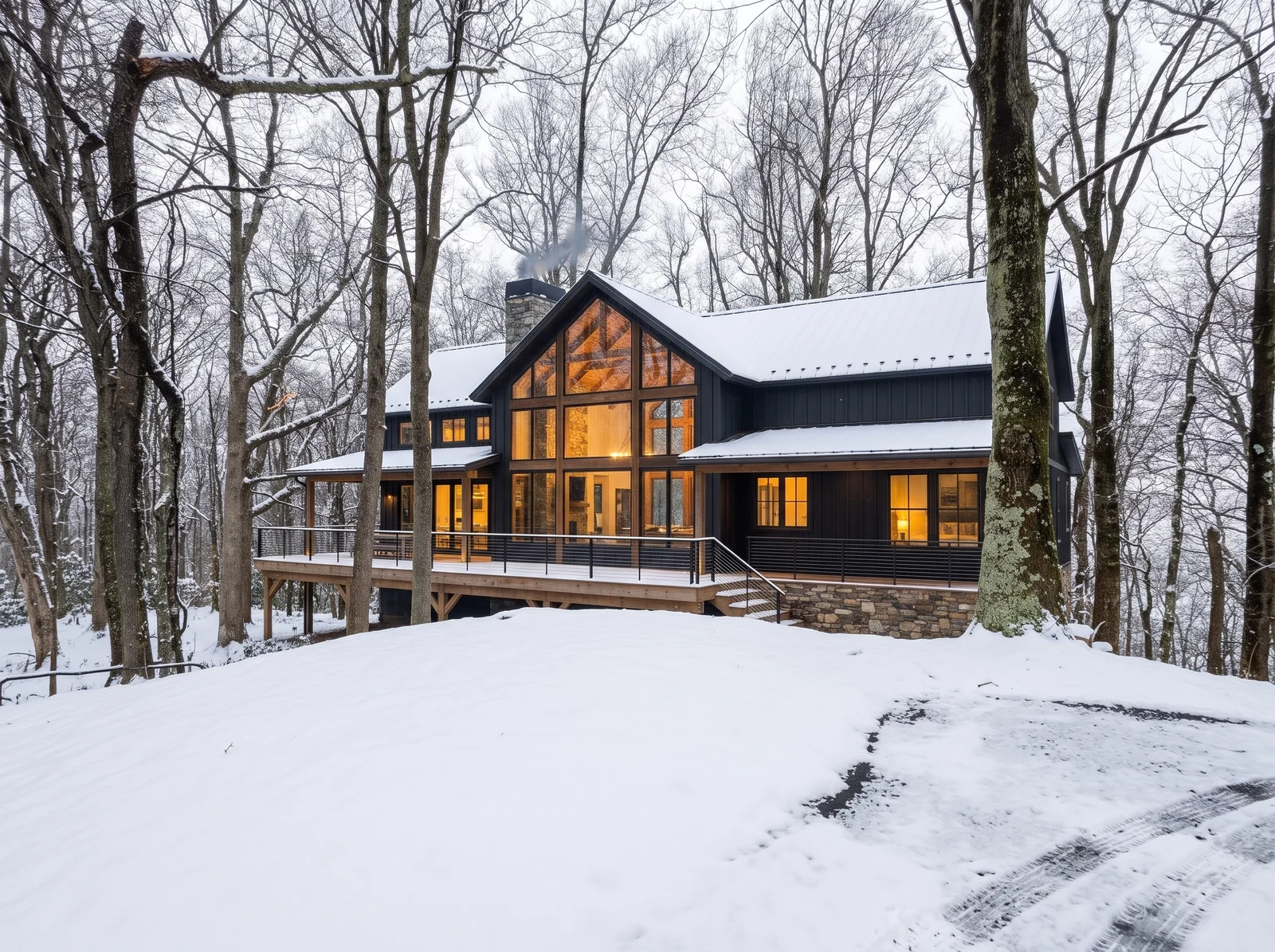 Concept rendering: the same house seen from the end of the drive after a snowfall, with smoke from the stone chimney, a lit glass gable and a large deck on timber posts